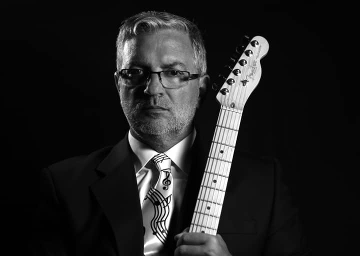 Grayscale portrait of a mature musician with an electric guitar in a studio setting.