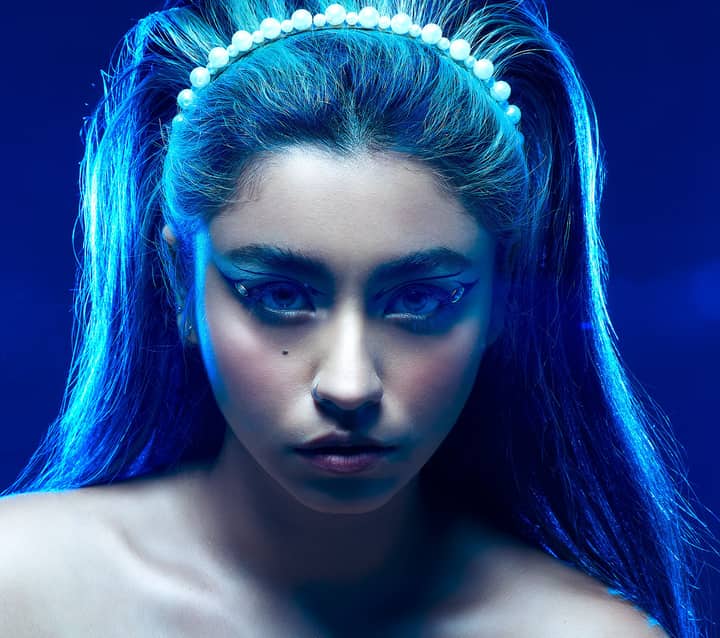 Creative studio portrait of a woman with striking artistic makeup and vibrant blue lighting.