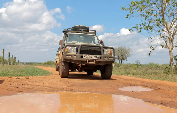 A rugged 4x4 SUV navigating a muddy outdoor trail under a bright sky.