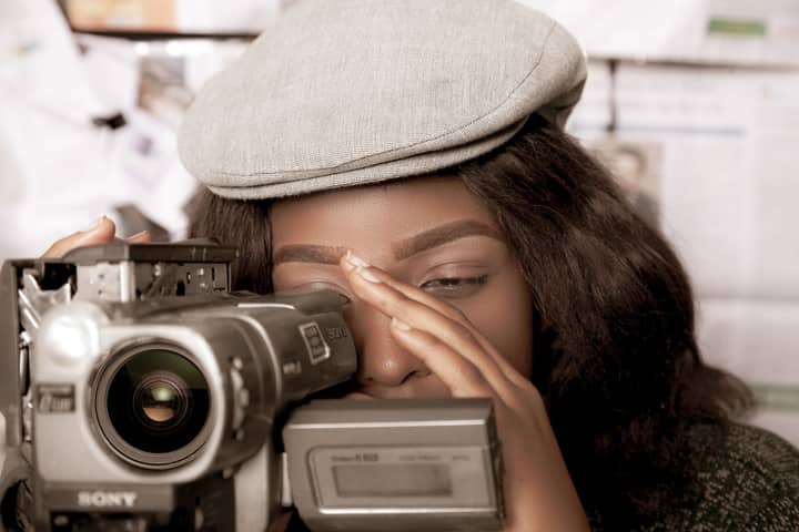 Black woman in vintage style filming with video camera, evoking a retro feel in Kampala.