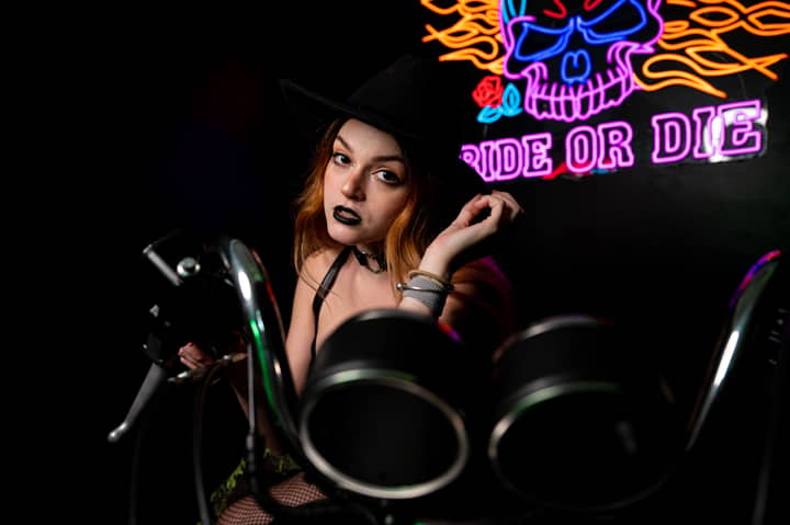 Captured moment of a woman in dark makeup near a neon sign and motorcycle.