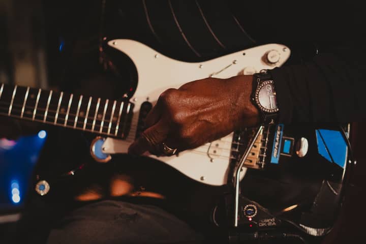 A detailed shot of a musician's hand playing an electric guitar in a New York City setting.