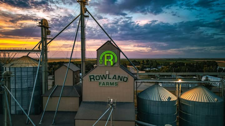 Aerial view of Rowland Farms with silos and industrial structures against a vibrant sunset in Taber, Alberta, Canada.