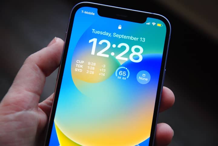 Close-up of a hand holding a smartphone showing a vibrant lock screen with time and date details.