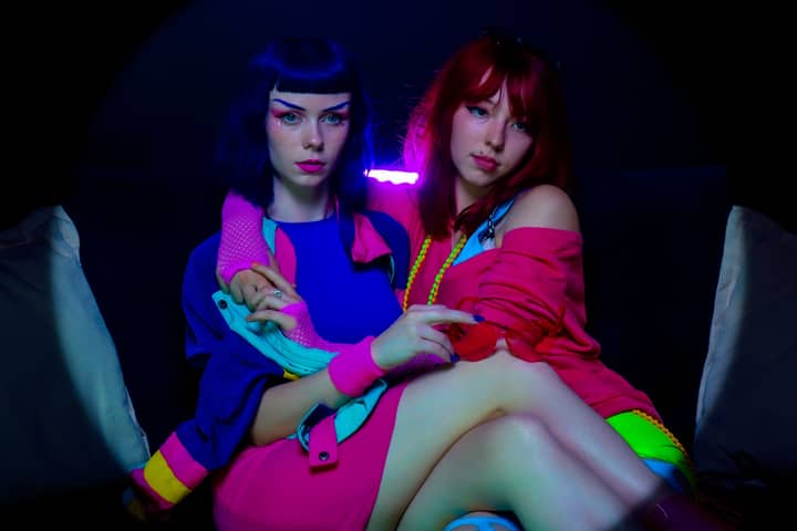 Bright neon lighting highlights two fashionable women sitting together.