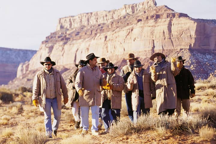 A group of men hiking in a desert canyon wearing casual western attire, enjoying a sunny day.
