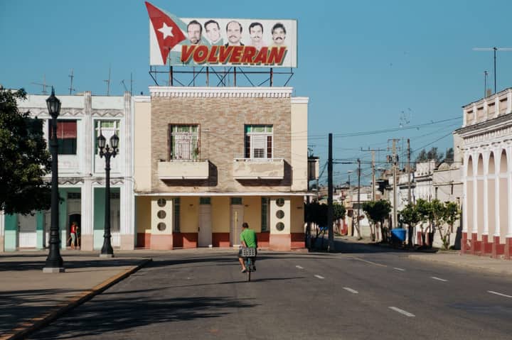 A cyclist rides past a colorful facade in a quiet Cuban town during summer.