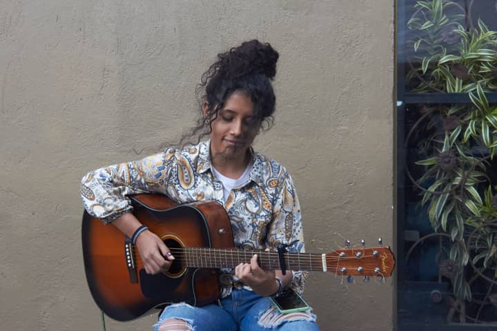 A young woman performs with an acoustic guitar against a textured wall in Bogotá.