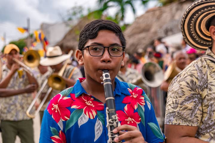 A vibrant street parade in Sincé, Colombia featuring young musicians playing clarinets.