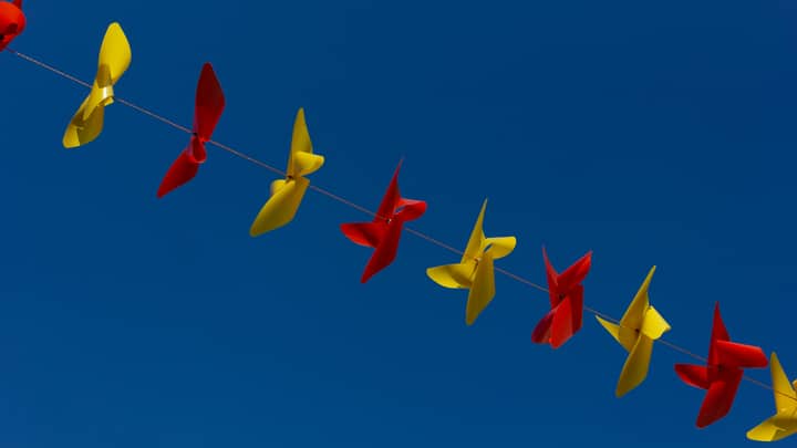 String of vibrant red and yellow pinwheels set against a clear blue sky, creating a lively and cheerful scene.