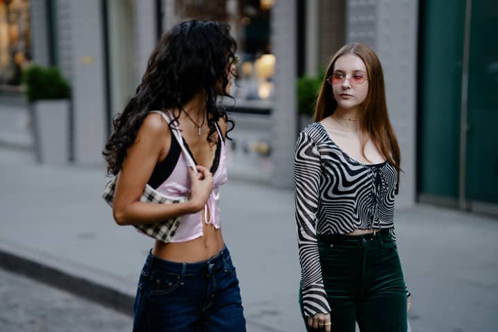Young fashionable women walking on urban street, showcasing trendy outfits.
