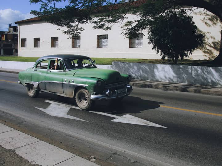 Classic green car on city street under blue sky, showcasing timeless automotive design.