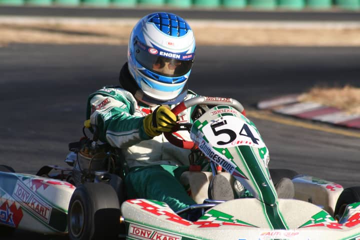 Driver in a go-kart navigating a racetrack, showcasing high-speed motorsport action.