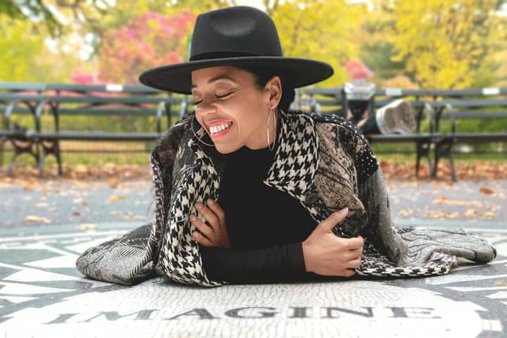 Cheerful woman in hat and hoop earrings lying on Imagine mosaic with autumn leaves in the background.
