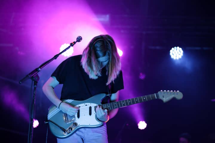 A captivating guitarist performs in vibrant lighting at a live concert in Breda, Netherlands.