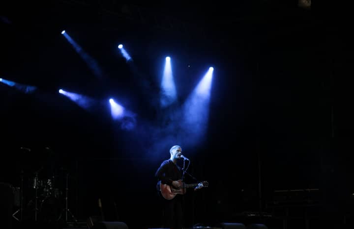 Solo musician performs on stage with guitar under dramatic blue lighting during a live concert.