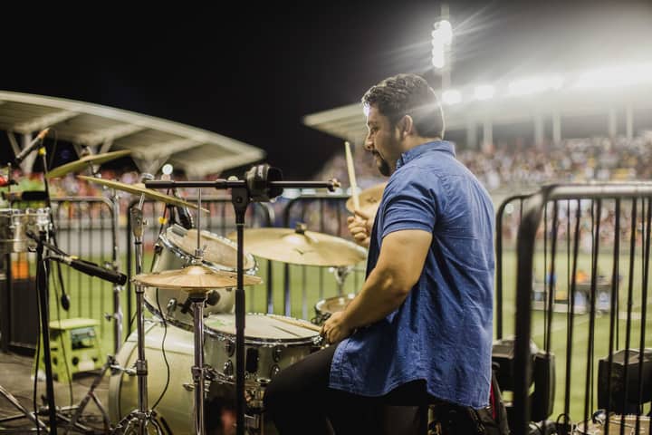 A drummer in a blue shirt playing live at a night concert with a full audience.