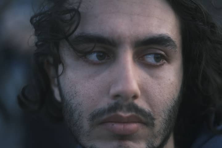 A close-up shot of a young man with curly hair and facial hair, looking thoughtful.