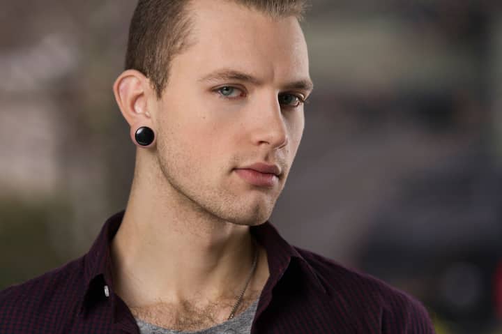 A portrait of a stylish man with earrings, exuding confidence and serious expression outdoors.
