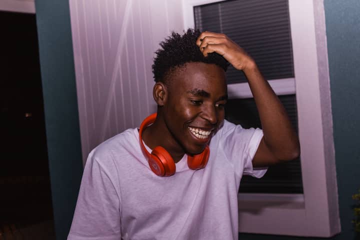 A cheerful young man wearing headphones, smiling indoors, exuding joy and happiness.