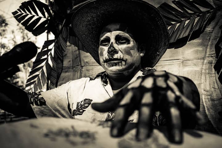 Black and white artistic portrait of a man with skull face paint wearing a hat and costume.