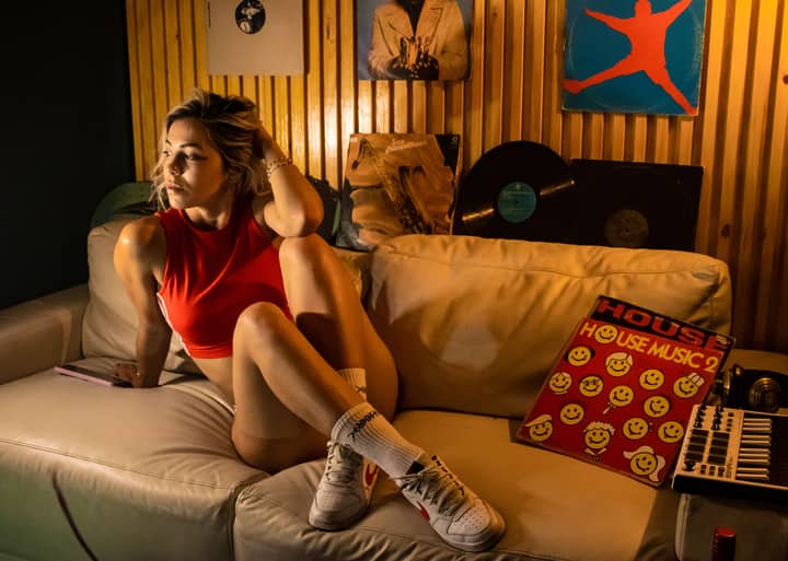 A fashionable woman sitting on a sofa surrounded by vinyl records in a cozy music room.