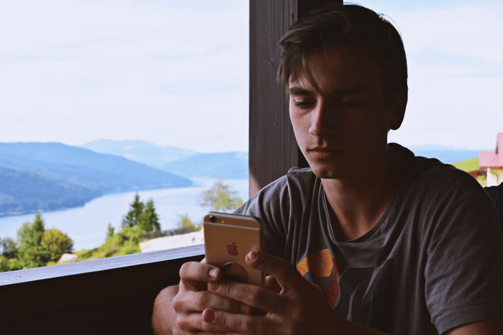 A young man using his smartphone while relaxing by a beautiful lakeside view in Bicaz, Romania.