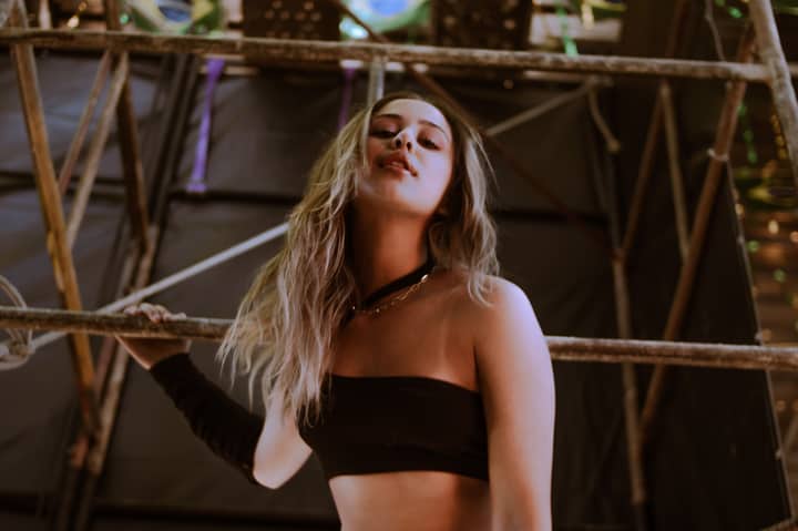 Stylish portrait of a blonde woman posing in a black tube top against scaffolding indoors.