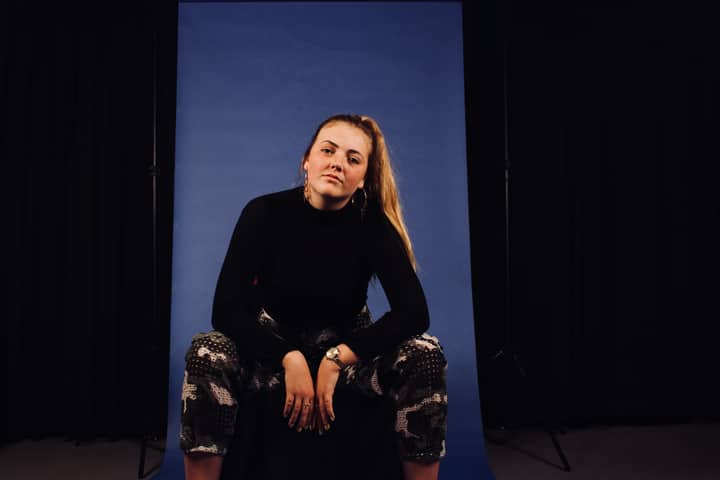 A stylish woman in a studio with a blue backdrop, exuding confidence and elegance.