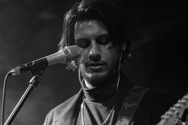 Black and white close-up of a male singer with a microphone, captured in a moody, artistic style.