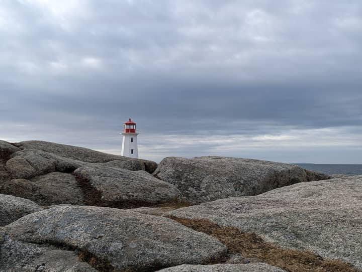 Iconic lighthouse at Peggy's Cove, Nova Scotia, stands amidst rugged rocks under a cloudy sky.