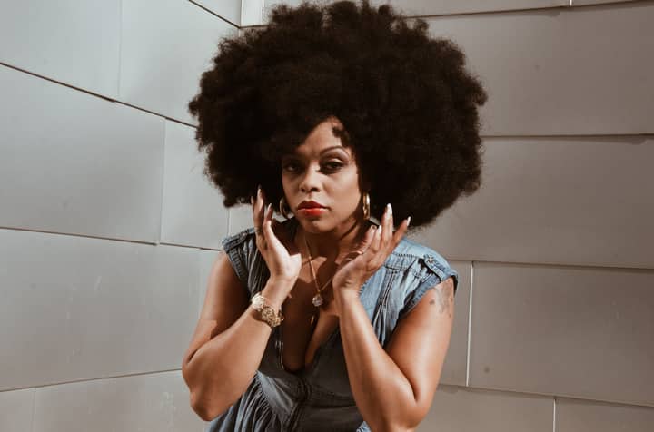 Portrait of a stylish Black woman with afro hair in a denim outfit against a modern wall.