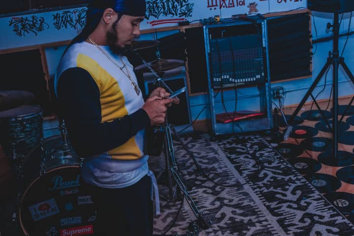 Musician in a studio setting using a smartphone, surrounded by instruments and records.