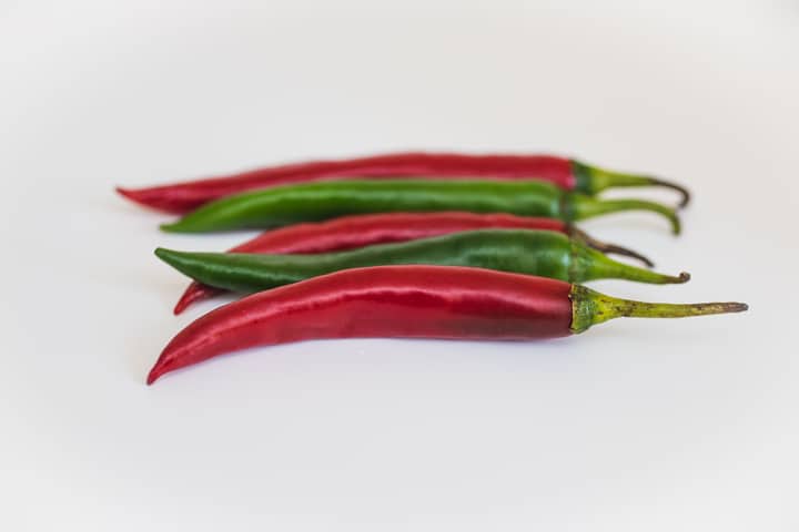 A close-up view of fresh red and green chili peppers placed on a white background.