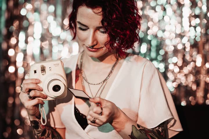 Woman holding a Polaroid camera with a bokeh background, wearing a white shirt.
