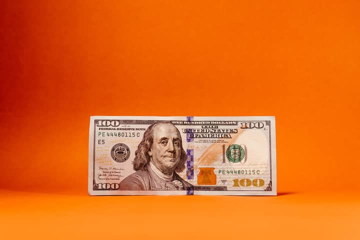 Crisp US hundred-dollar bill against a vivid orange backdrop. Ideal for finance themes.