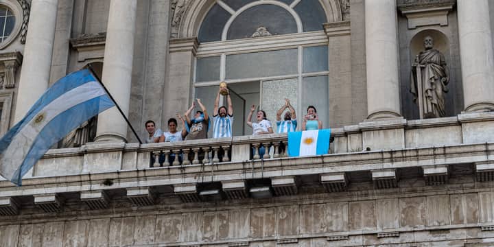 People celebrating with flags and a trophy on a Buenos Aires balcony.