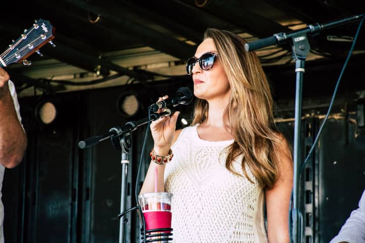 A woman in sunglasses sings on stage during an outdoor concert, exuding confidence and style.