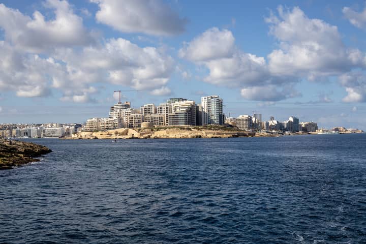 A scenic view of a coastal city skyline with blue skies and scattered clouds.