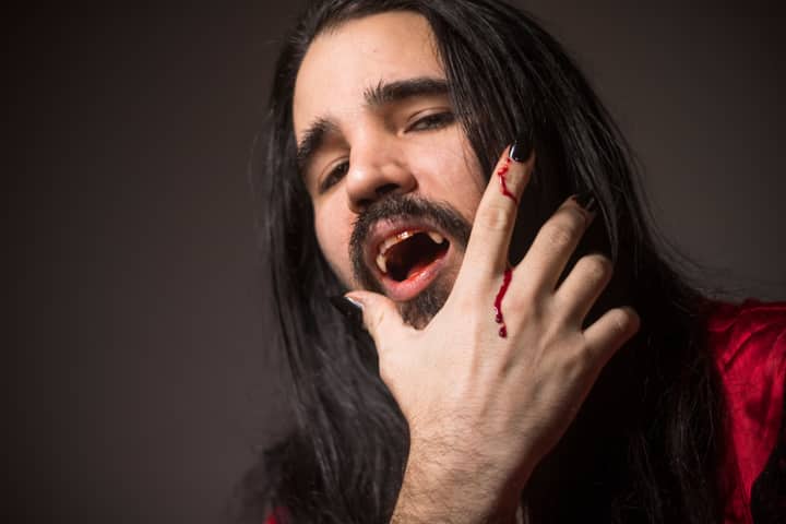 Close-up portrait of a man in vampire cosplay with fangs and bloodied hand.