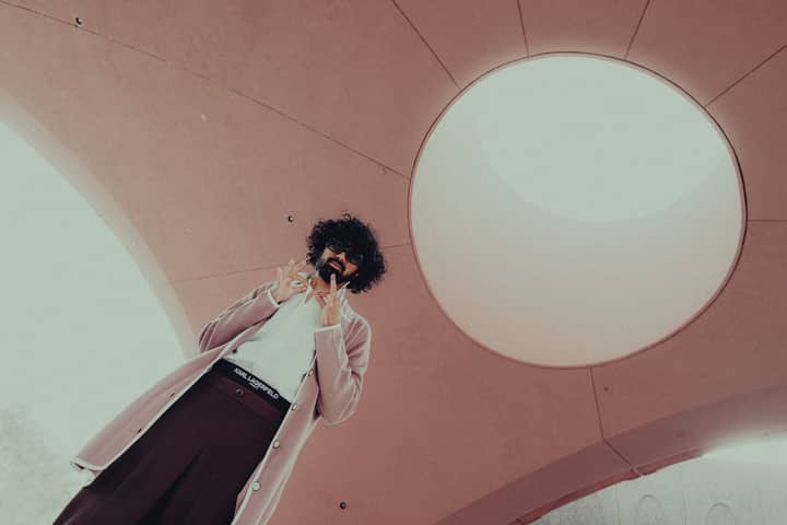 Fashionable man with sunglasses poses under a dome with unique architecture.