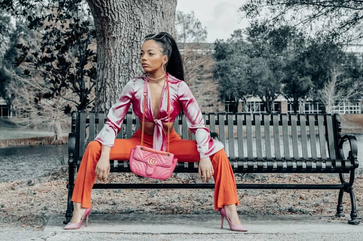 Fashionable woman sitting on a metal bench in vibrant attire outdoors.