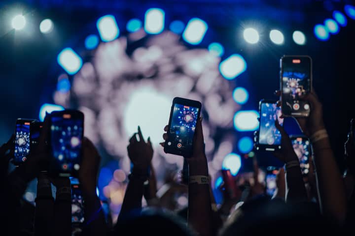 Attendees film a vibrant concert stage with smartphones capturing the mesmerizing lights.