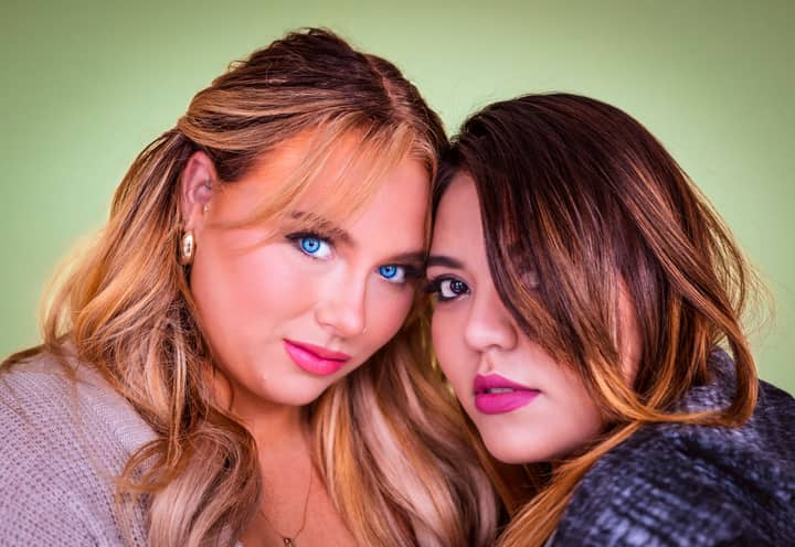 Intimate portrait of two women with long hair against a green background, showcasing beauty and friendship.