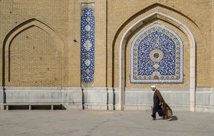 Middle-Eastern man walking past a beautifully decorated mosque wall in Qom, Iran.