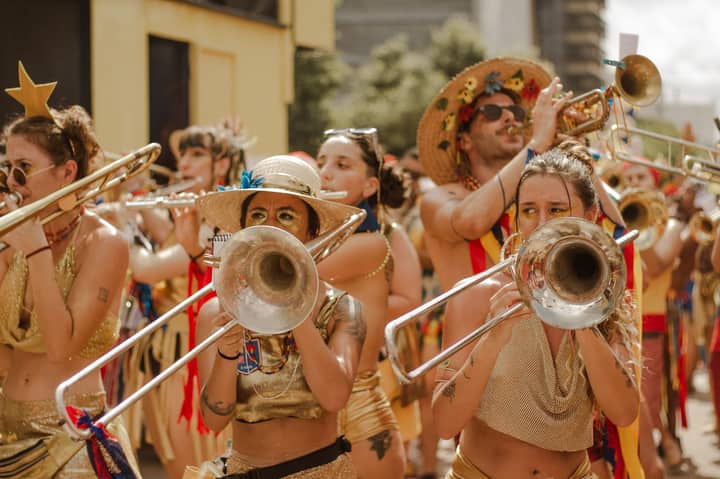 Colorful street parade featuring musicians in festive attire playing brass instruments outdoors.