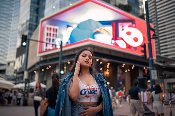 Fashionable young woman posing in an urban city street with colorful billboards in background.