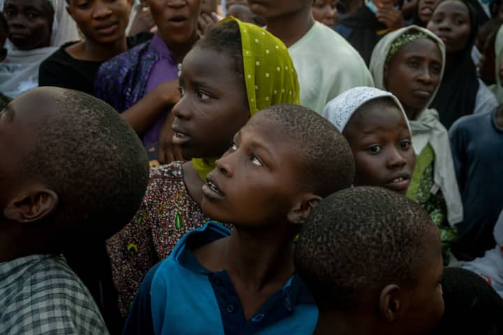 A diverse group of children looking up in curiosity amidst a crowd, evoking a sense of anticipation.