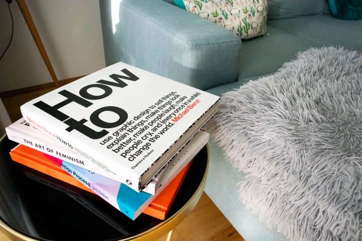 Modern living room with a pile of design and art books on a black coffee table, next to a cozy couch with pillows.