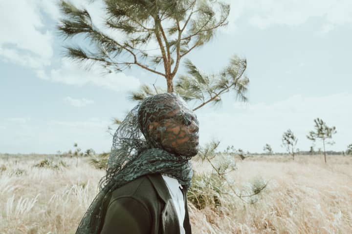 Unique fashion portrait of a man in sunglasses and veil in a rural grassland.